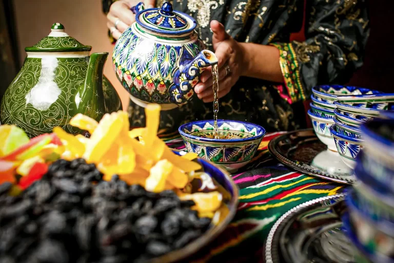 Женщина наливает чай из узбекского чайника в декоративную пиалу.