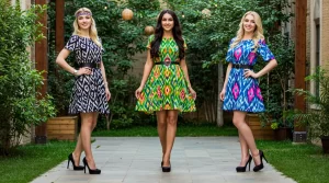 Три девушки в платьях из икатовой ткани на улице, зелёный фон. Three women in ikat dresses, street, green background.